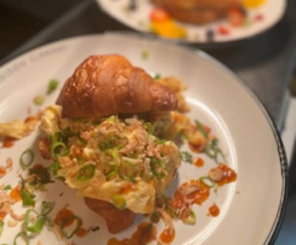 Close-up of a plated dish featuring a pastry or croissant topped with savory ingredients like green onions and possibly seafood.