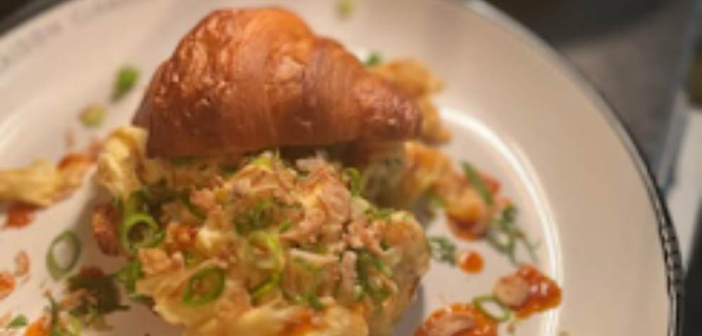 Close-up of a plated dish featuring a pastry or croissant topped with savory ingredients like green onions and possibly seafood.