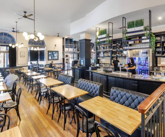 Cozy restaurant or café interior with wooden tables and chairs, a bar counter, and shelves stocked with bottles.