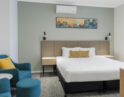 Hotel room featuring a single large bed, bedside tables with lamps, modern decor, and a seating area with chairs.
