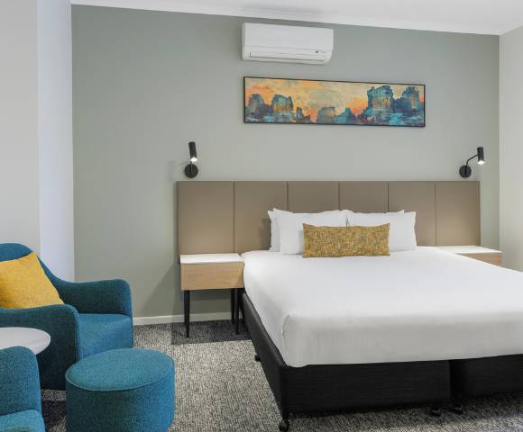 Hotel room featuring a single large bed, bedside tables with lamps, modern decor, and a seating area with chairs.
