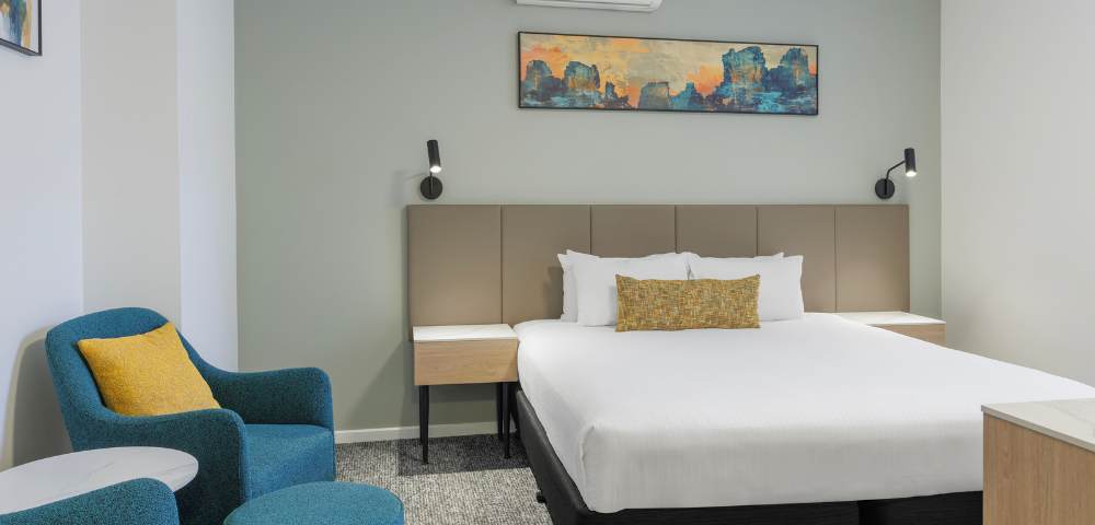 Hotel room featuring a single large bed, bedside tables with lamps, modern decor, and a seating area with chairs.