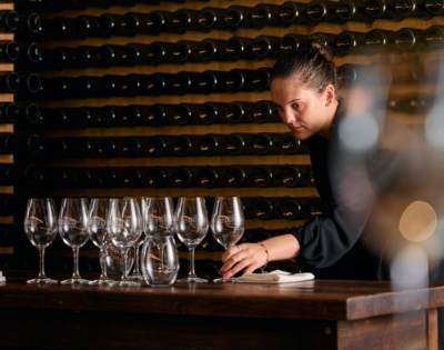 Person arranging multiple empty wine glasses on a table, likely preparing for a wine tasting session.