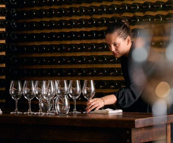 Person arranging multiple empty wine glasses on a table, likely preparing for a wine tasting session.