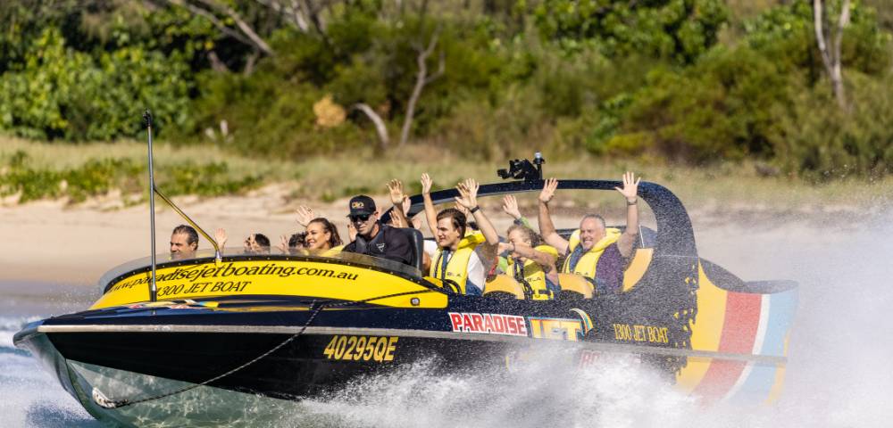 Jet boat gliding over water with scenic background and visible branding.