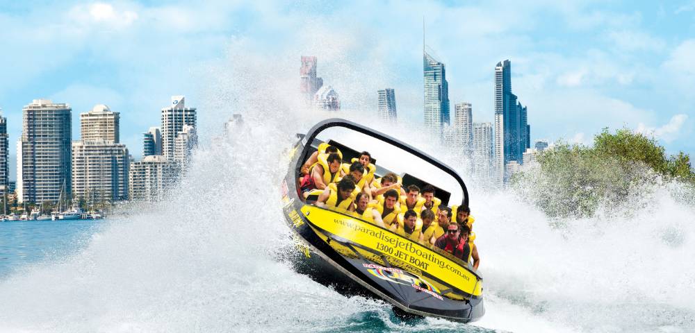 Jet boat performing stunts near towering city buildings, showcasing urban adventure.