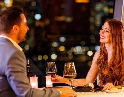 Two people enjoying drinks at a restaurant table with blurred city lights in the background.