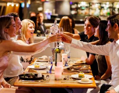 Group of people clinking glasses over a meal in a lively restaurant setting.