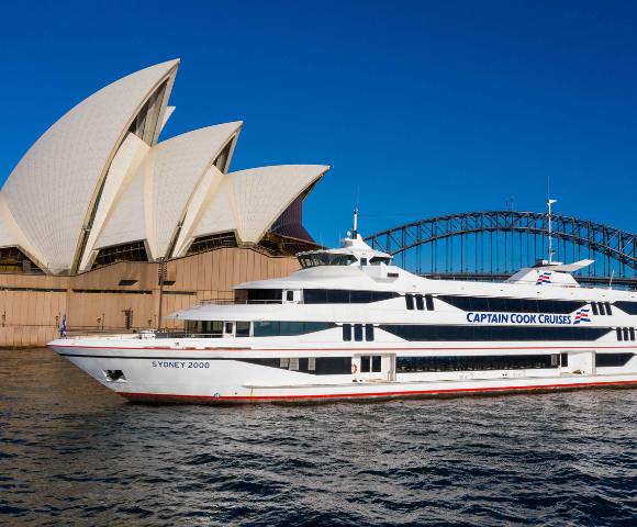 Sydney Opera House and a large yacht on calm waters under clear blue skies