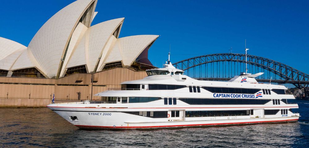Sydney Opera House and a large yacht on calm waters under clear blue skies