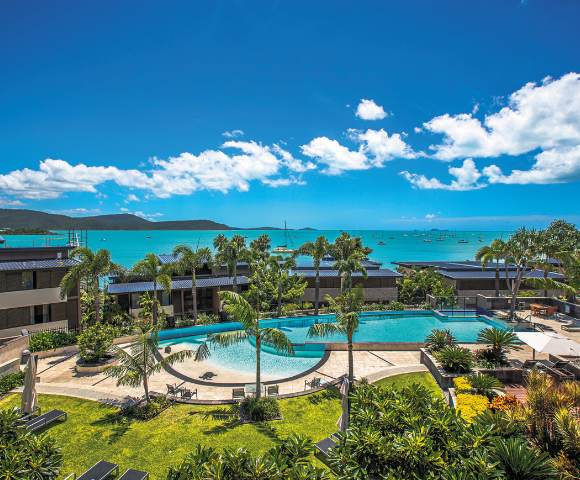 Identical panoramic view of resort pools and ocean vistas under blue skies.