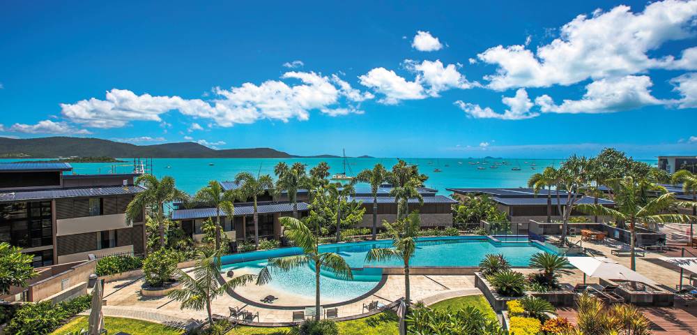 Identical panoramic view of resort pools and ocean vistas under blue skies.