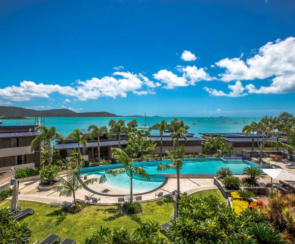Panoramic view of multiple resort pools extending toward the ocean under bright skies.