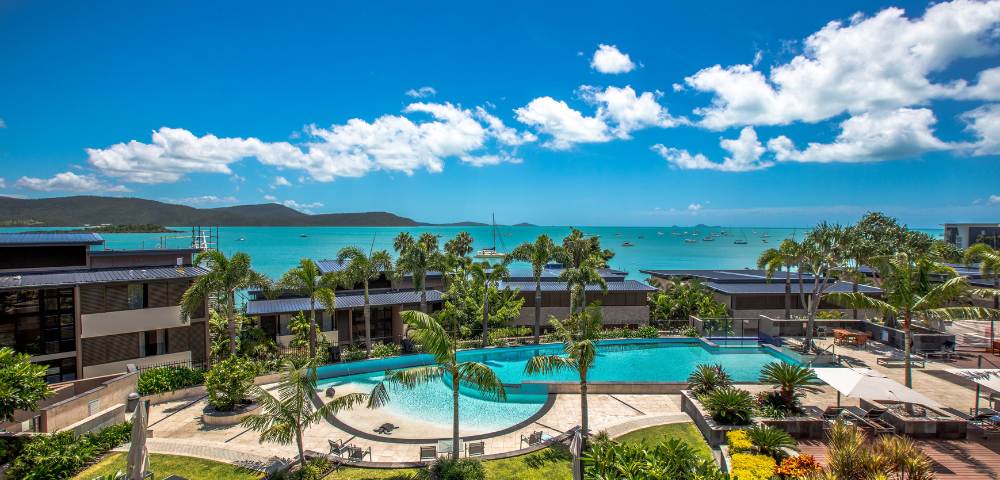 Panoramic view of multiple resort pools extending toward the ocean under bright skies.