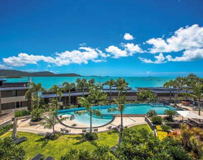 Identical panoramic view of resort pools and ocean vistas under blue skies.