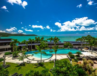 Elevated view of a resort pool area with surrounding greenery and distant ocean views.
