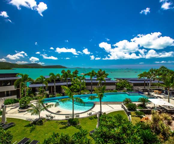 Elevated view of a resort pool area with surrounding greenery and distant ocean views.