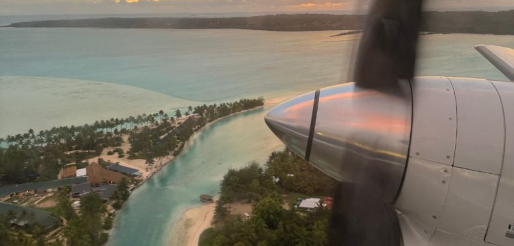 Aerial view of turquoise waters and palm-lined shores at sunset, with a propeller in the foreground highlighting the serene tropical landscape.
