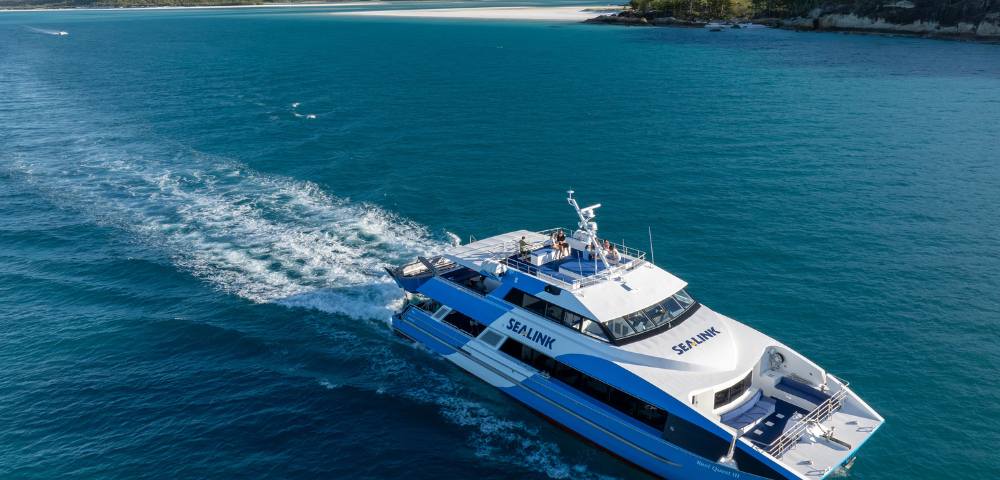 A large boat cruising through clear blue waters with an island in the background.