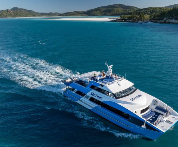 A large boat cruising through clear blue waters with an island in the background.