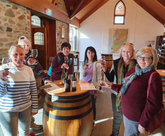Two people smiling at the camera while standing at a table with wine glasses and bottles.
