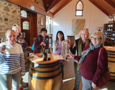 Two people smiling at the camera while standing at a table with wine glasses and bottles.