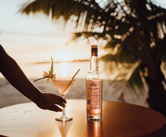 Bottle of liquor on an outdoor table at sunset, with palm trees and ocean in the background.