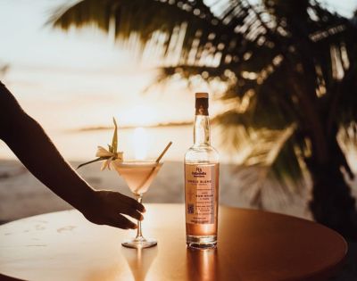 Bottle of liquor on an outdoor table at sunset, with palm trees and ocean in the background.