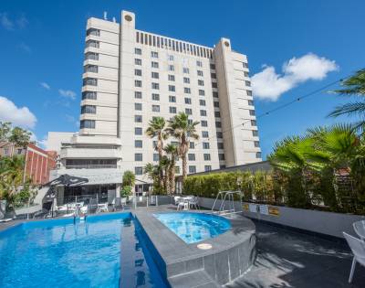 Outdoor pool area at Hotel Grand Chancellor Adelaide surrounded by lounge chairs, palm trees, and greenery.