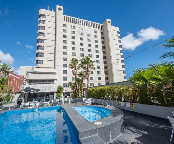 Outdoor pool area at Hotel Grand Chancellor Adelaide surrounded by lounge chairs, palm trees, and greenery.