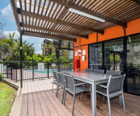 Outdoor BBQ area with seating and grill facilities surrounded by greenery.