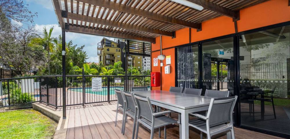 Outdoor BBQ area with seating and grill facilities surrounded by greenery.