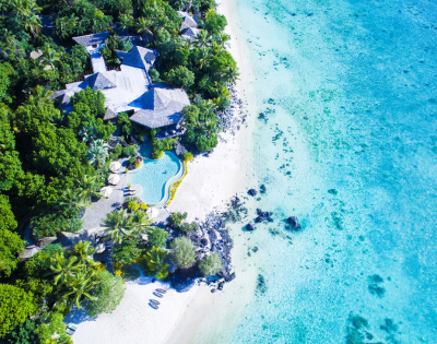 The image features a beautiful beach with a large swimming pool situated in the middle of the scene. The pool is surrounded by a variety of palm trees, creating a tropical atmosphere. There are several chairs placed around the pool area, providing a comfortable spot for relaxation.