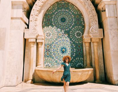 A person stands in front of a beautifully tiled Moroccan fountain adorned with intricate geometric patterns.