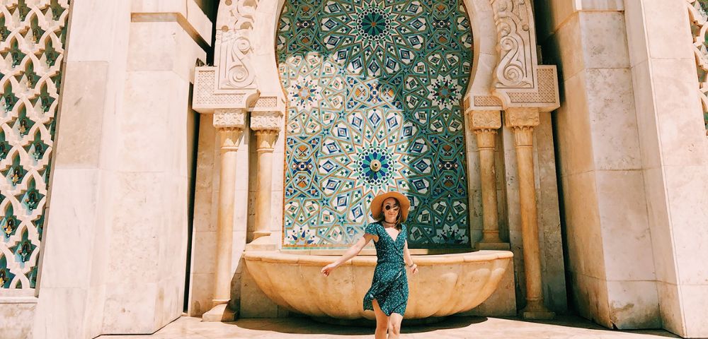 A person stands in front of a beautifully tiled Moroccan fountain adorned with intricate geometric patterns.