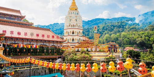Colorful lanterns adorned a temple complex with traditional red-tiled roofs and a tall white pagoda, set against a lush green mountain backdrop.