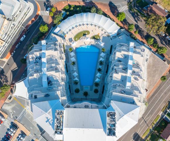 Aerial view of Mantra Ettalong Beach resort featuring a large swimming pool and surrounding buildings