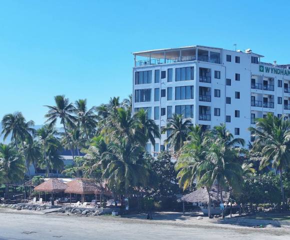 A multi-story building close to the shore, surrounded by trees and overlooking a body of water.
