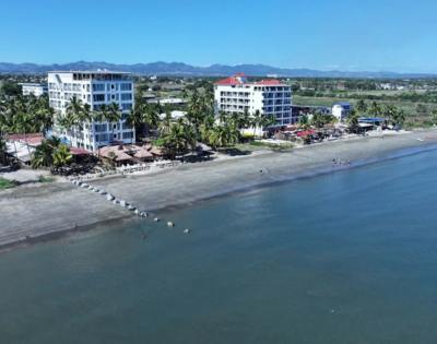 Wide-angle aerial view of a coastal region with multiple buildings and greenery.