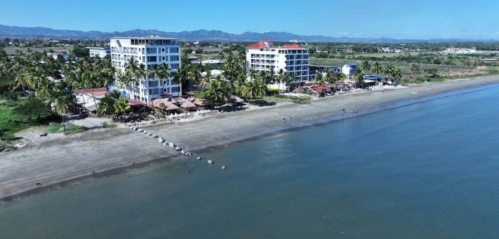 Wide-angle aerial view of a coastal region with multiple buildings and greenery.