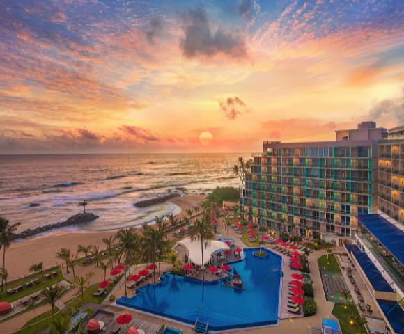 Aerial view of the hotel property at sunset, highlighting the pool area, surrounding greenery, and beachside location.