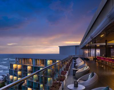 Rooftop bar with seating arrangements overlooking the ocean at sunset, offering a scenic and relaxing atmosphere