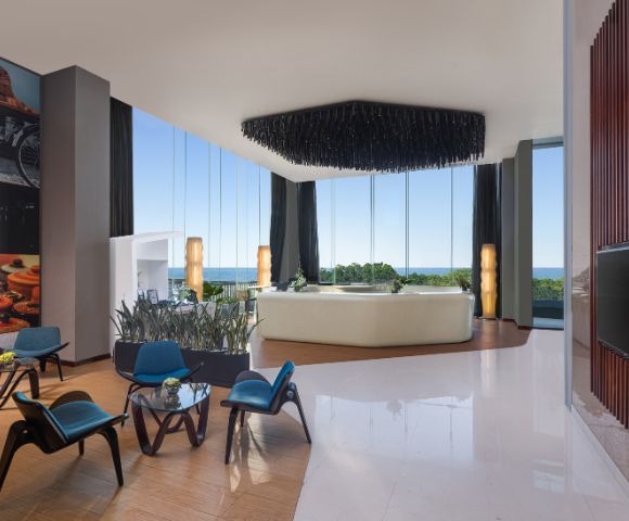 Comfortably furnished hotel living space with seating, a coffee table, decorative accents, and large windows providing natural light