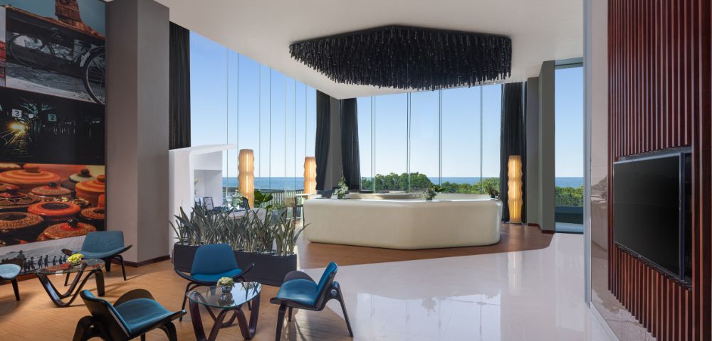 Comfortably furnished hotel living space with seating, a coffee table, decorative accents, and large windows providing natural light