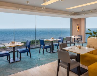 Elegant dining space with tables and chairs, overlooking the ocean through large windows, offering a scenic and relaxing atmosphere