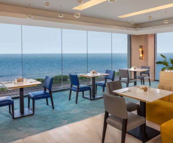 Elegant dining space with tables and chairs, overlooking the ocean through large windows, offering a scenic and relaxing atmosphere