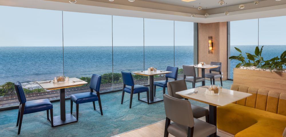 Elegant dining space with tables and chairs, overlooking the ocean through large windows, offering a scenic and relaxing atmosphere