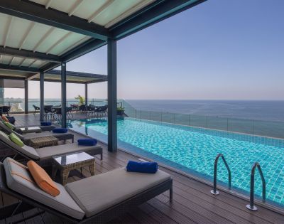 Outdoor infinity pool with lounge chairs under a shaded canopy, overlooking the ocean for a luxurious and tranquil experience.