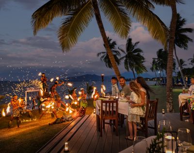 Outdoor dining setup with tables and chairs overlooking the ocean at sunset.