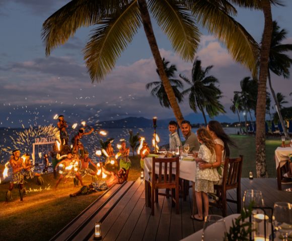 Outdoor dining setup with tables and chairs overlooking the ocean at sunset.